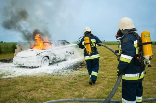 firefighters putting out a fire on a car in a field